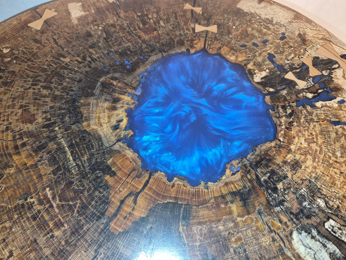 Table basse hêtre échauffé et résine bleue, piètement en métal.

Le plateau est issue d'une tranche de hêtre échauffé dont le milieu était creux, une bonne raison d'y ajouter de la résine !&nbsp;

Les noeuds papillons en chêne bien qu'ésthétiques sont aussi là pour empêcher que les fentes dans le bois ne progressent davantages.

La résine bleue métalisée donne de magnifiques reflets peu importe comment nous regardons la table.