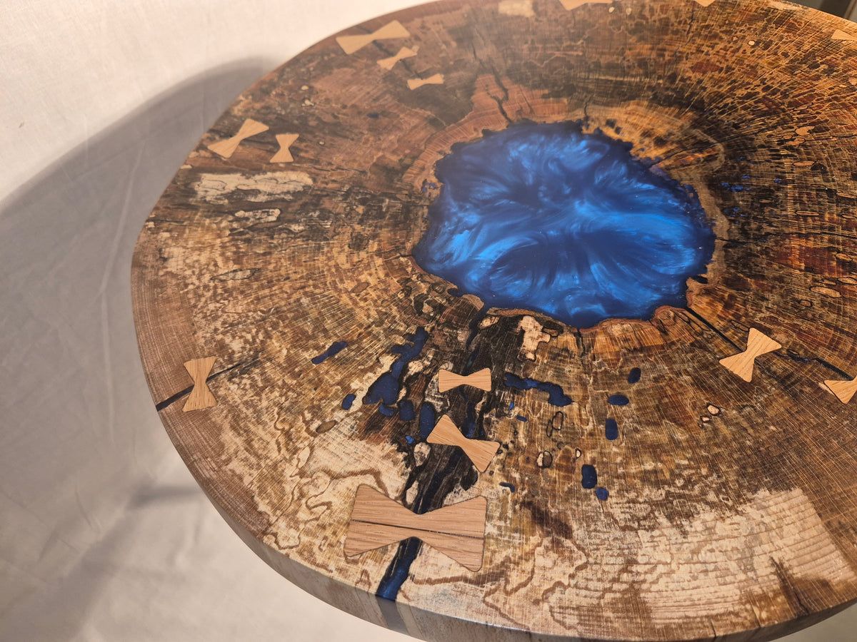 Table basse hêtre échauffé et résine bleue, piètement en métal.

Le plateau est issue d'une tranche de hêtre échauffé dont le milieu était creux, une bonne raison d'y ajouter de la résine !&nbsp;

Les noeuds papillons en chêne bien qu'ésthétiques sont aussi là pour empêcher que les fentes dans le bois ne progressent davantages.

La résine bleue métalisée donne de magnifiques reflets peu importe comment nous regardons la table.