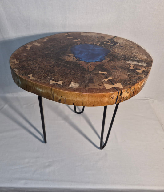 Table basse hêtre échauffé et résine bleue, piètement en métal.

Le plateau est issue d'une tranche de hêtre échauffé dont le milieu était creux, une bonne raison d'y ajouter de la résine !&nbsp;

Les noeuds papillons en chêne bien qu'ésthétiques sont aussi là pour empêcher que les fentes dans le bois ne progressent davantages.

La résine bleue métalisée donne de magnifiques reflets peu importe comment nous regardons la table.