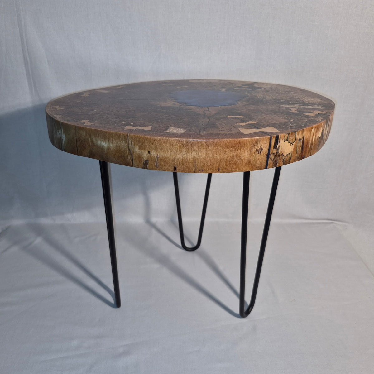 Table basse hêtre échauffé et résine bleue, piètement en métal.


Le plateau est issue d'une tranche de hêtre échauffé dont le milieu était creux, une bonne raison d'y ajouter de la résine !&nbsp;

Les noeuds papillons en chêne bien qu'ésthétiques sont aussi là pour empêcher que les fentes dans le bois ne progressent davantages.

La résine bleue métalisée donne de magnifiques reflets peu importe comment nous regardons la table.