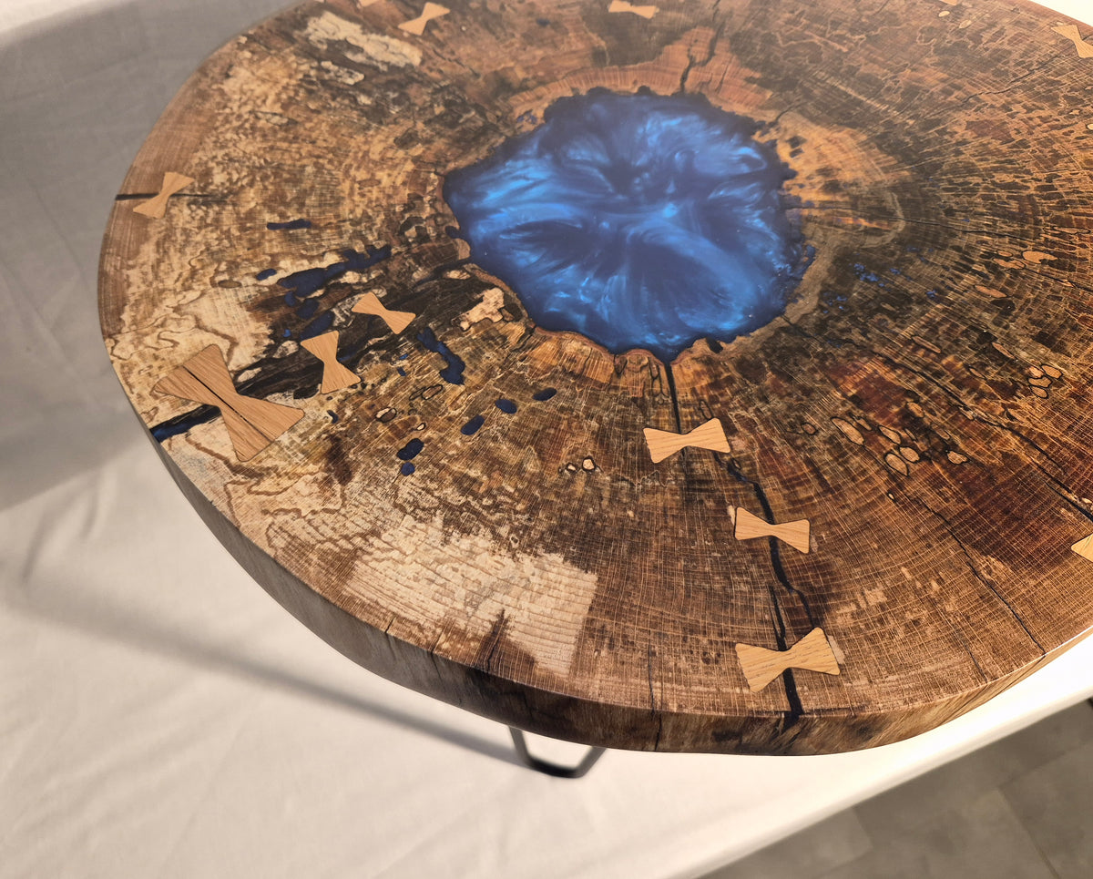 Table basse hêtre échauffé et résine bleue, piètement en métal.

Le plateau est issue d'une tranche de hêtre échauffé dont le milieu était creux, une bonne raison d'y ajouter de la résine !&nbsp;

Les noeuds papillons en chêne bien qu'ésthétiques sont aussi là pour empêcher que les fentes dans le bois ne progressent davantages.

La résine bleue métalisée donne de magnifiques reflets peu importe comment nous regardons la table.